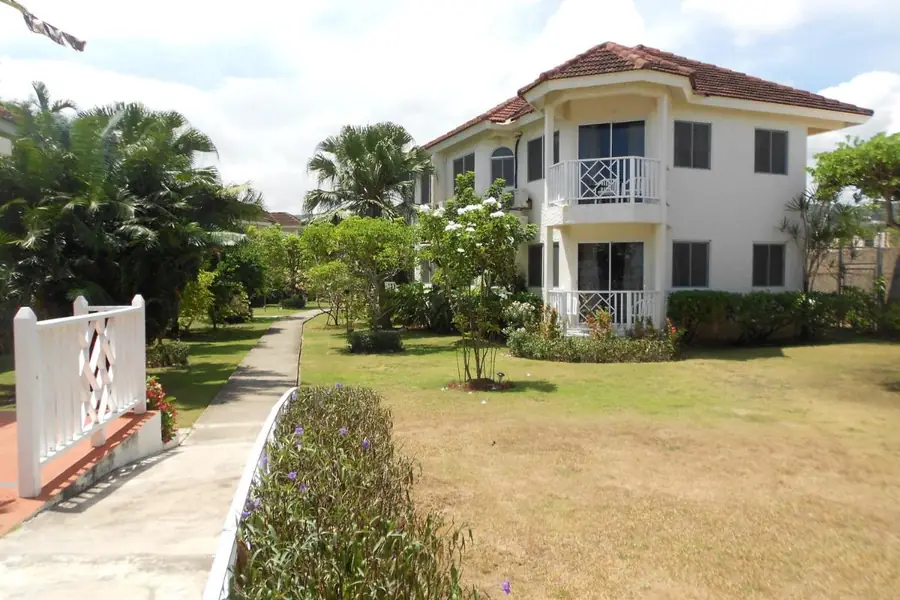 Een van de gebouwen van Pipers Cove Resort, twee verdiepingen met balkons, tussen palmbomen en tuin